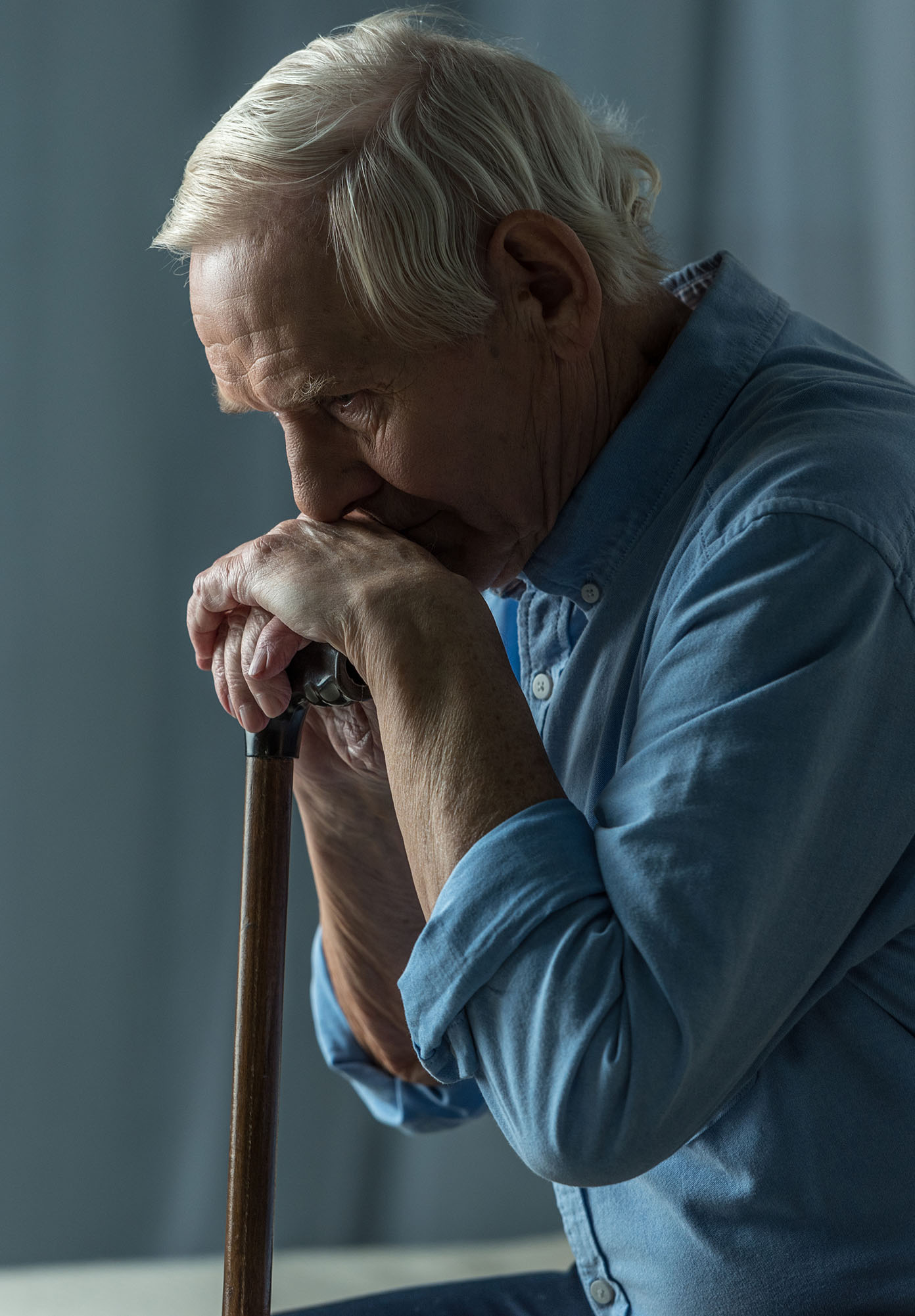 Senior sad man leans on a cane while sitting on sofa